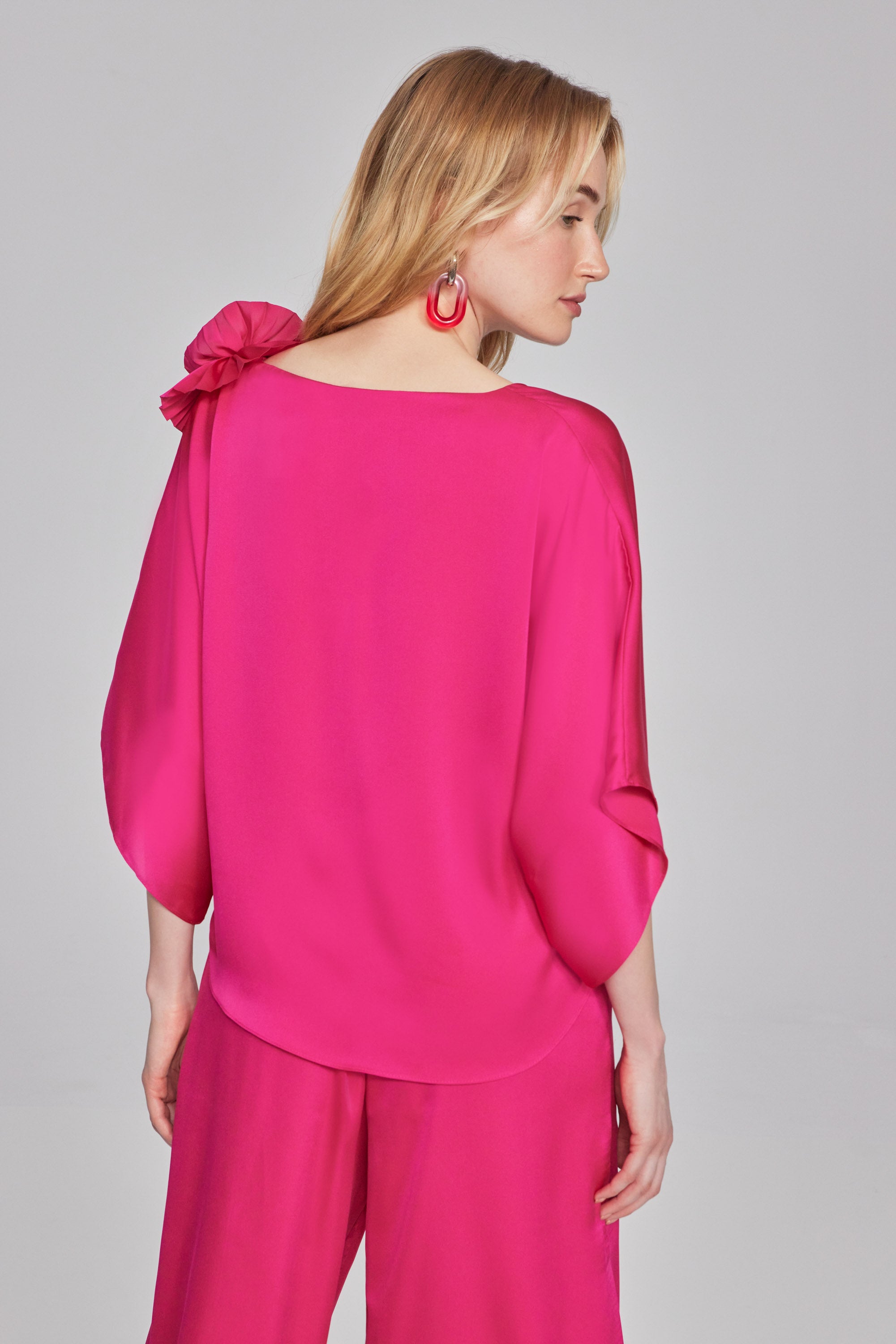 This satin flared top is where elegance meets whimsy. The pleated rosette detail at the shoulder adds a playful and unique touch. The three-quarter dolman sleeves and V-shaped neckline add to its allure, making it a standout piece in your wardrobe. Part of the Signature Collection.